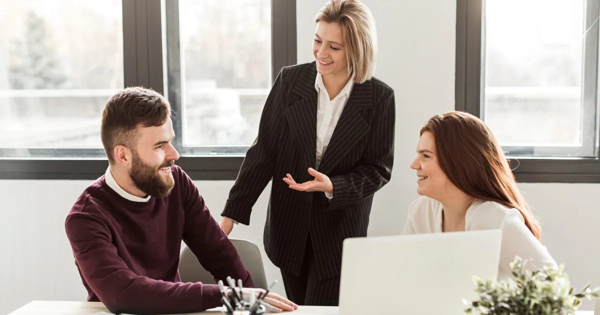 Three business professionals engaged in a friendly conversation in a modern office setting.